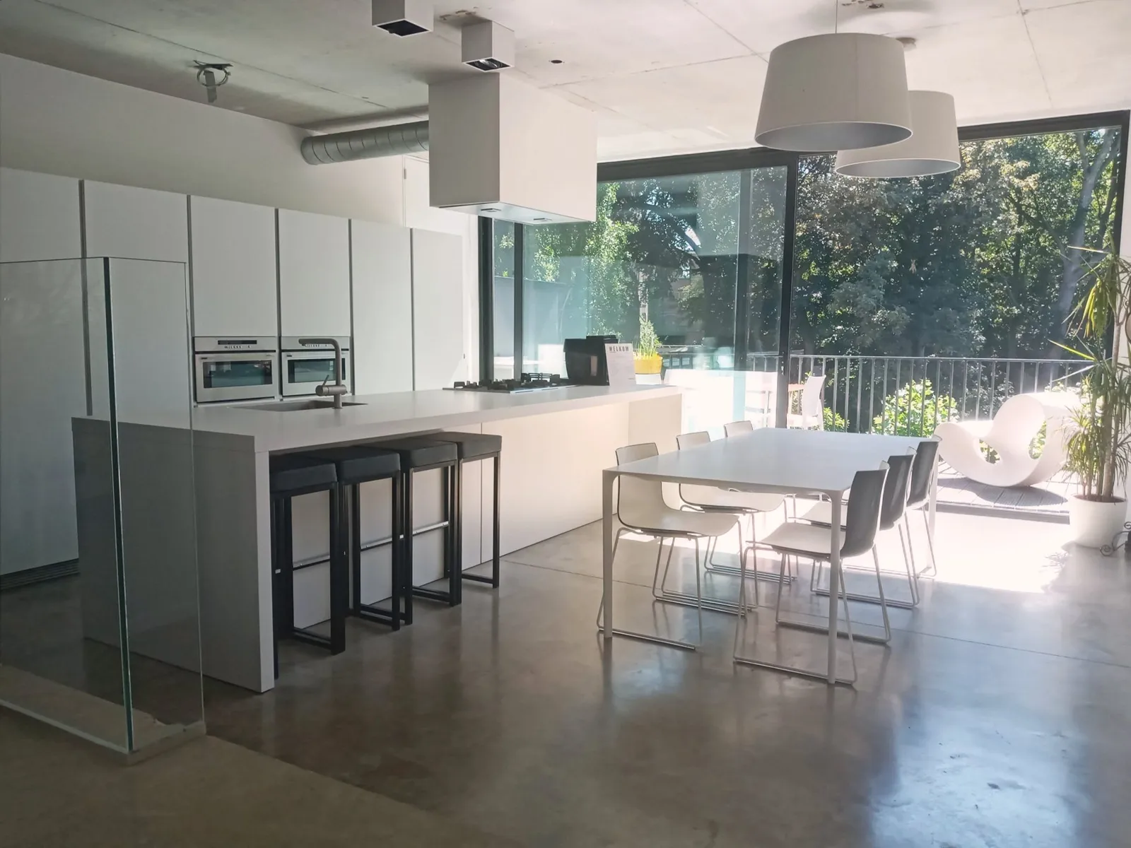 White kitchen island and dining table opening onto the terrace and the trees of ’t Groen Kwartier